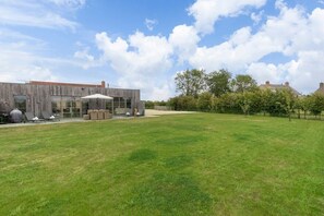 A modern building with a grassy yard and a patio area with outdoor furniture.