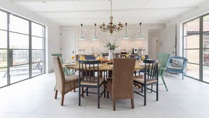 A dining area with a large table, wicker chairs, and hanging pendant lights.