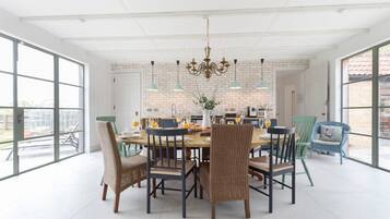 A dining area with a large table, wicker chairs, and hanging pendant lights.