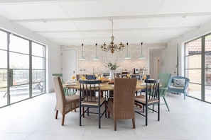A dining area with a large table, wicker chairs, and hanging pendant lights.