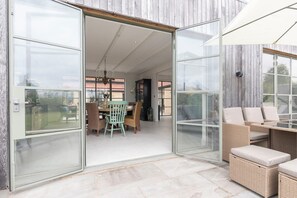 A modern house with a glass door leading to an interior dining area with a table and chairs.