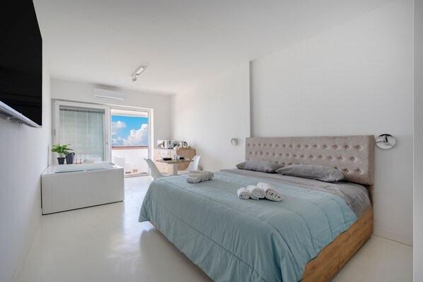 A modern bedroom with a large bed, a desk, and a view of the sky.