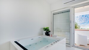 A modern bathroom with a large bathtub, a glass door leading to an outdoor area, and a potted plant. - Holiday Home 'Angel Suite 2' with Balcony, Wi-Fi and Air Conditioning (Selva di Fasano)