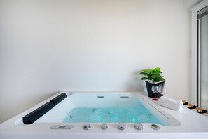 A modern bathroom with a bathtub, a control panel, a potted plant, and two wine glasses.