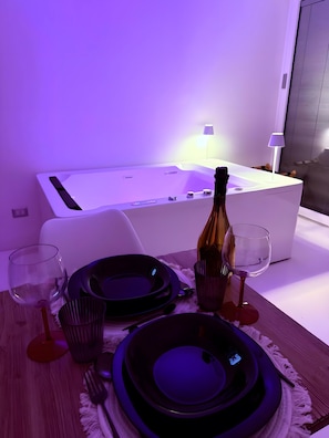 A modern room with a white bathtub, a bottle of champagne, and dining set on a wooden table.