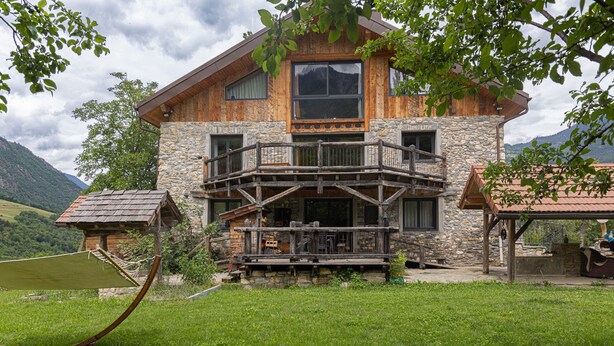 A wooden cabin with a stone facade, a balcony, and a grassy yard. - Chalet La Sentinelle – Alpine Elegance, Comfort, and Nature in the Heart of Tarentaise (Grand-Aigueblanche)