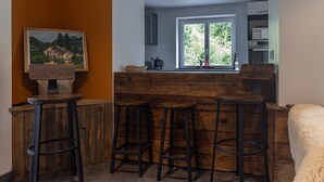 A kitchen with wooden stools, a window with a view, and a painting on the wall. - Chalet La Sentinelle – Alpine Elegance, Comfort, and Nature in the Heart of Tarentaise (Grand-Aigueblanche)