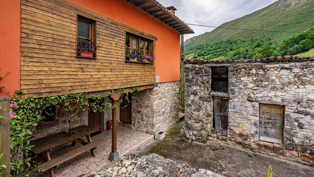 A rustic building with a wooden bench, stone walls, and a window with flowers. - Casa Rural Ricao with Mountain Views, Private Terrace and WiFi (Cangas de onis)