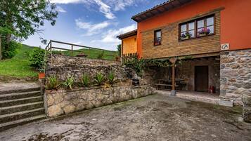 A rustic stone house with a wooden staircase, a stone wall with plants, and a wooden fence.