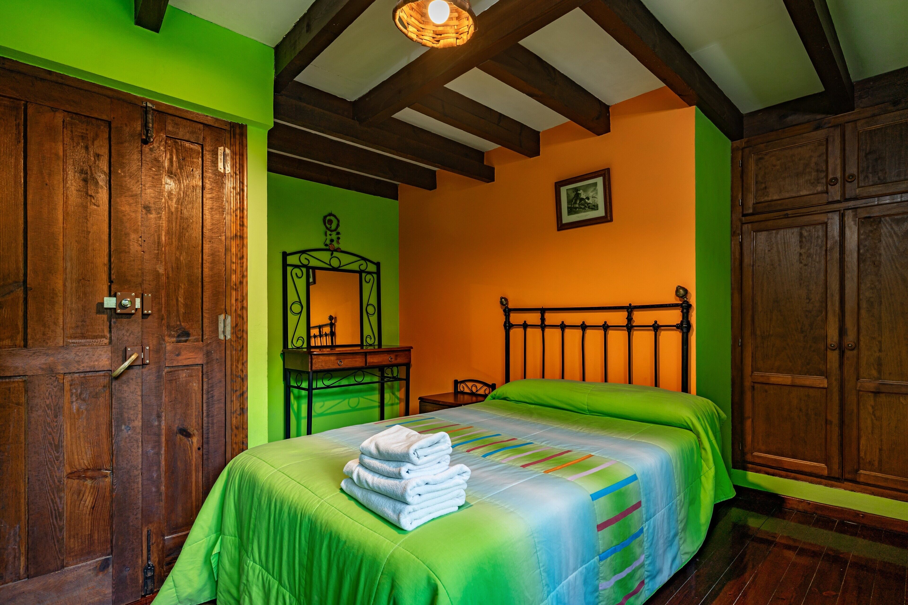 Habitació amb llit, armari de fusta i escriptori amb mirall.