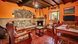 A cozy living room with a fireplace, wooden furniture, and a stone wall. - Casa Rural Ricao with Mountain Views, Private Terrace and WiFi (Cangas de onis)