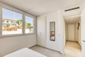 Un dormitorio con un ventanal grande, un armario, un espejo y una puerta que da a otra habitación.