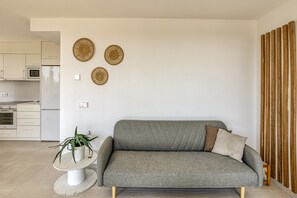 A modern living room with a grey sofa, a small round table with a potted plant, and three woven wall decorations.