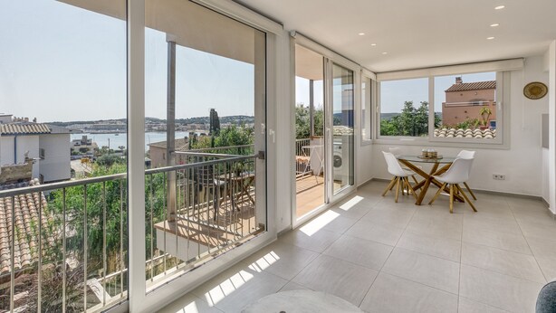 A modern interior with large sliding glass doors, a dining area with a round table and chairs, and a view of a coastal landscape. - Bright Apartment 100 m from the Beach – 1st Floor (L'Escala)