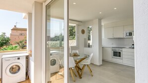 A modern kitchen with white cabinets, a dining table with chairs, and a washing machine in a balcony area. - Bright Apartment 100 m from the Beach – 1st Floor (L'Escala)