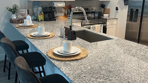 A modern kitchen with white cabinets, a granite countertop, a stainless steel refrigerator, and a built-in microwave. - Brand New Modern Corporate Rental in Eado (Houston)