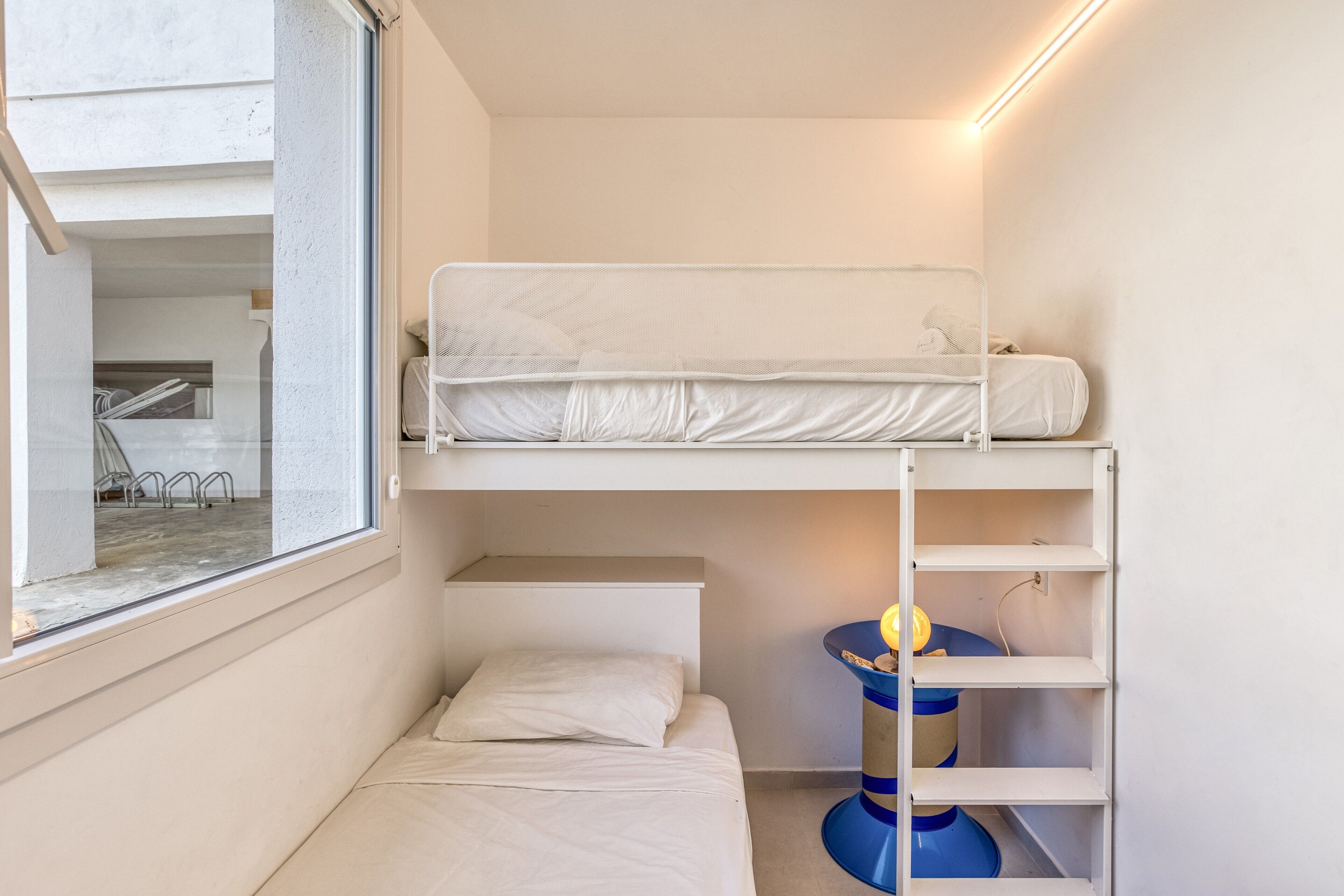 Habitación con literas, una ventana, un escritorio y una silla azul.