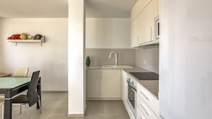 Eine moderne Küche mit weißen Schränken, einem eingebauten Backofen und einem Glastisch mit Stühlen.