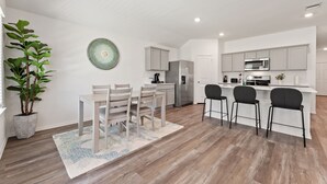 A modern kitchen with white cabinets, stainless steel appliances, and a dining area with a wooden table and chairs. - Brand-New 4BR Magnolia Retreat · Sleeps 8 · Fast WiFi · 30 Min to Woodlands (Magnolia)