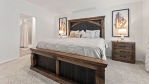A bedroom with a large bed, wooden headboard, two bedside tables with lamps, and a door leading to a bathroom. - Brand-New 4BR Magnolia Retreat · Sleeps 8 · Fast WiFi · 30 Min to Woodlands (Magnolia)