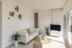 Een moderne woonkamer met een bank, een glazen salontafel, een televisie en decoratieve wandkunst.