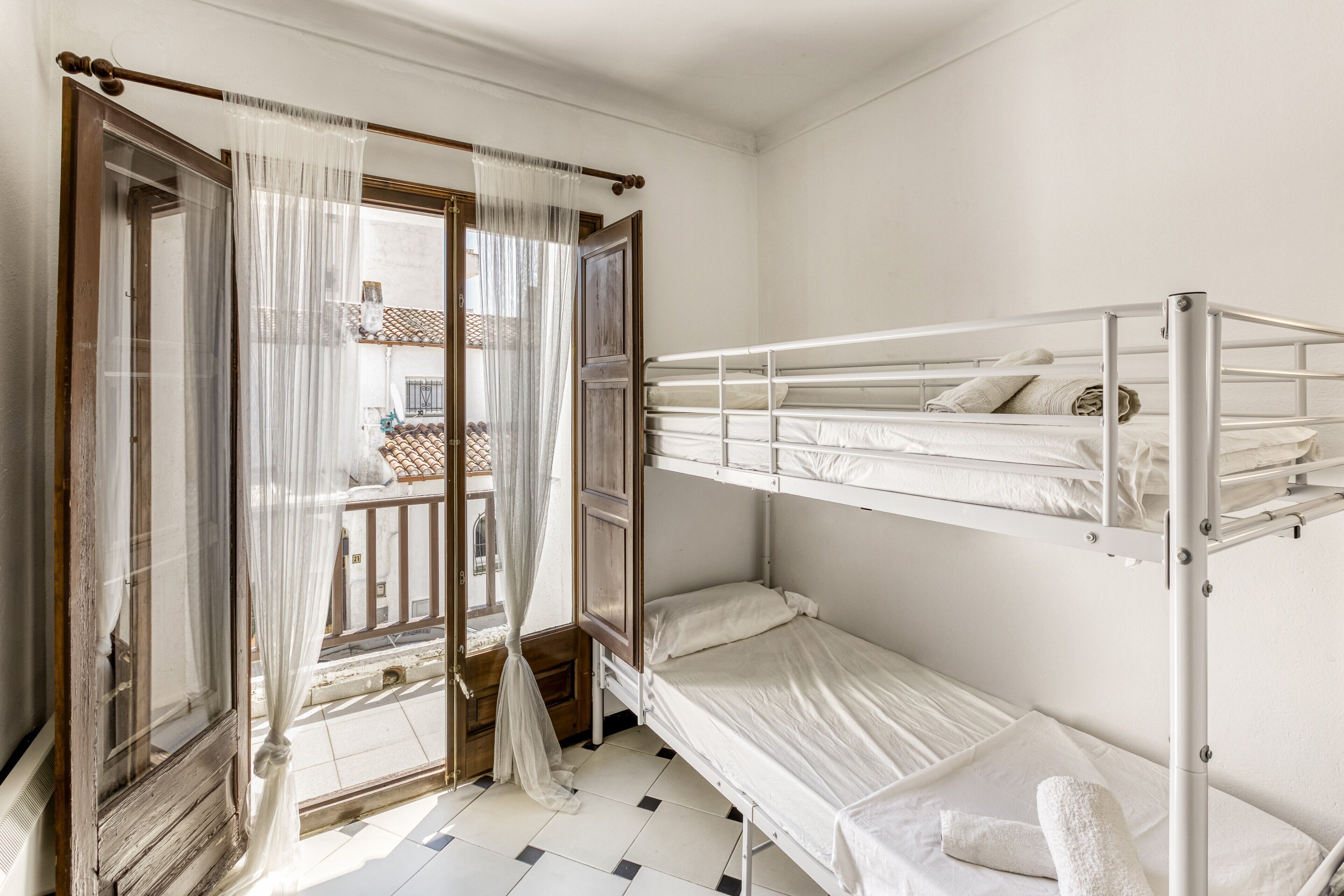 Une chambre avec un lit superposé, une fenêtre avec des rideaux légers et une vue sur un balcon.