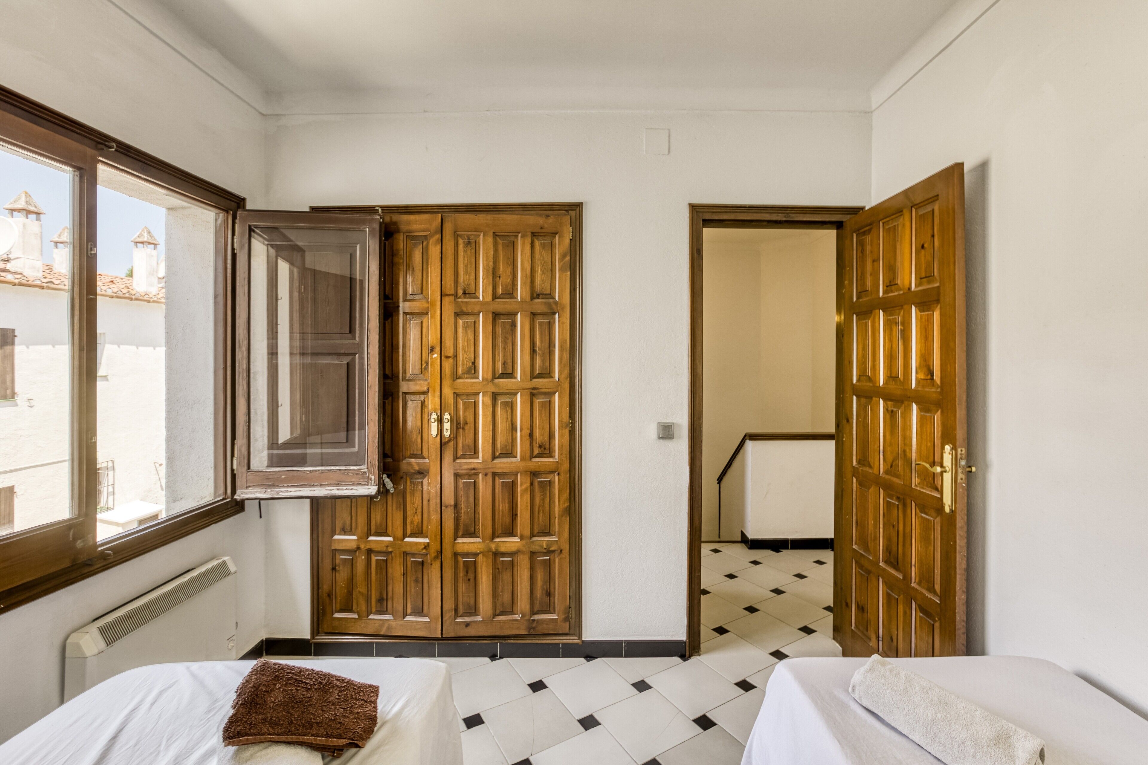 A room with two beds, a window, and a door leading to another room.