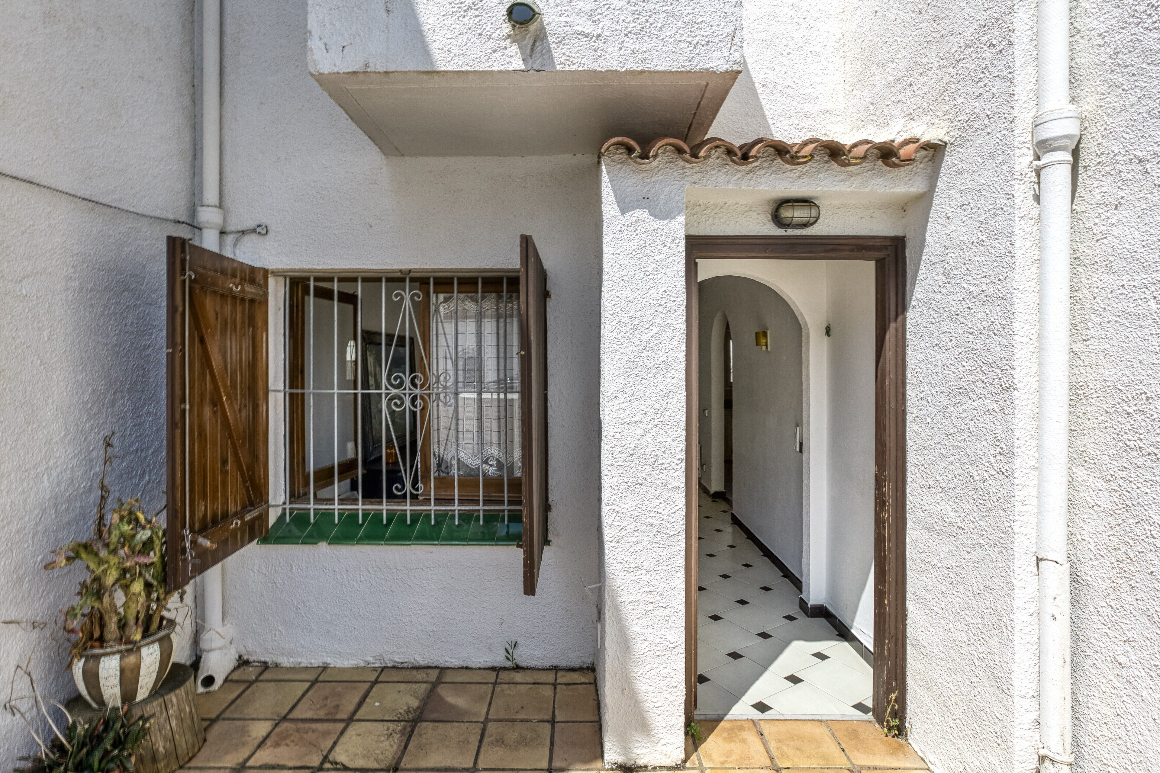 A narrow alleyway with a white building, a wooden door, and a window with a metal gate.