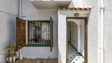 A narrow alleyway with a white building, a wooden door, and a window with a metal gate.