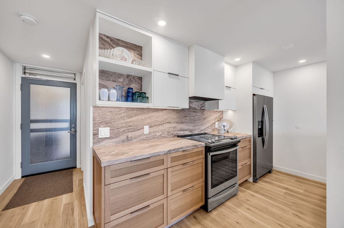Eine moderne Küche mit Holzschränken, einer Marmorarbeitsplatte, einem Edelstahlkühlschrank und einem Backofen.
