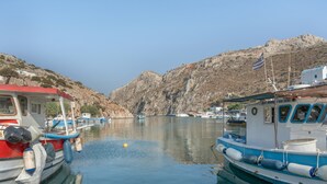 Una marina con barcos amarrados, agua tranquila y colinas rocosas al fondo.