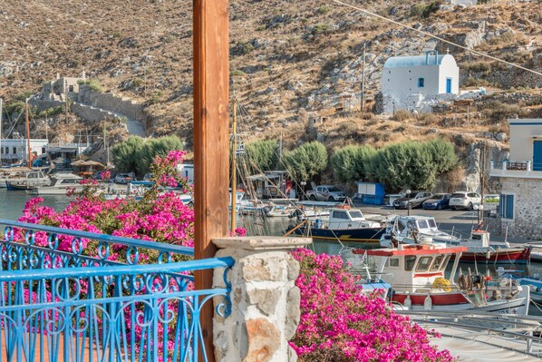 A coastal village with boats docked, a white building with a blue door, and a stone staircase leading up the hill.