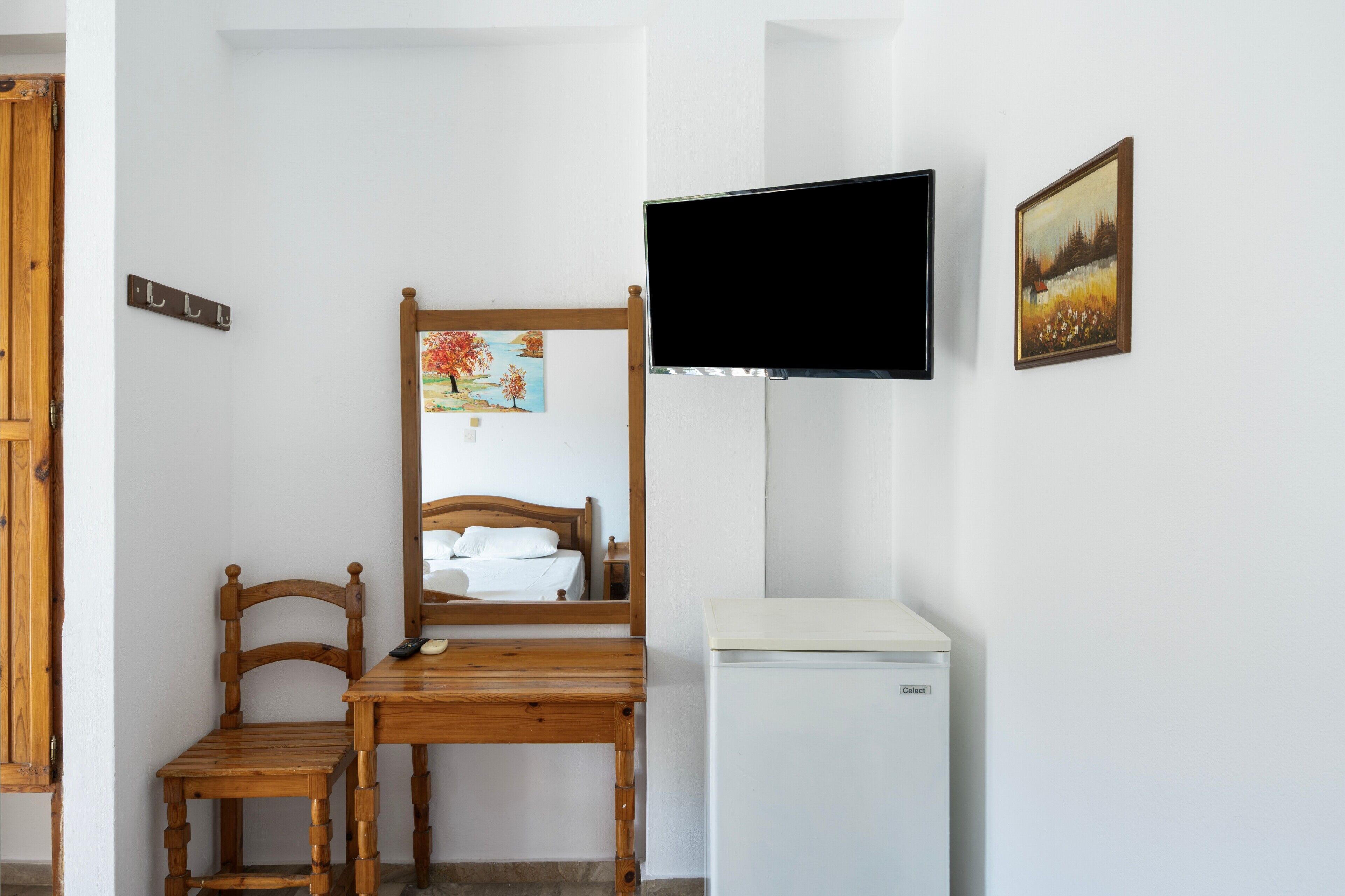 A bedroom with a wooden bed, a small table, a mirror, a television, and a refrigerator.