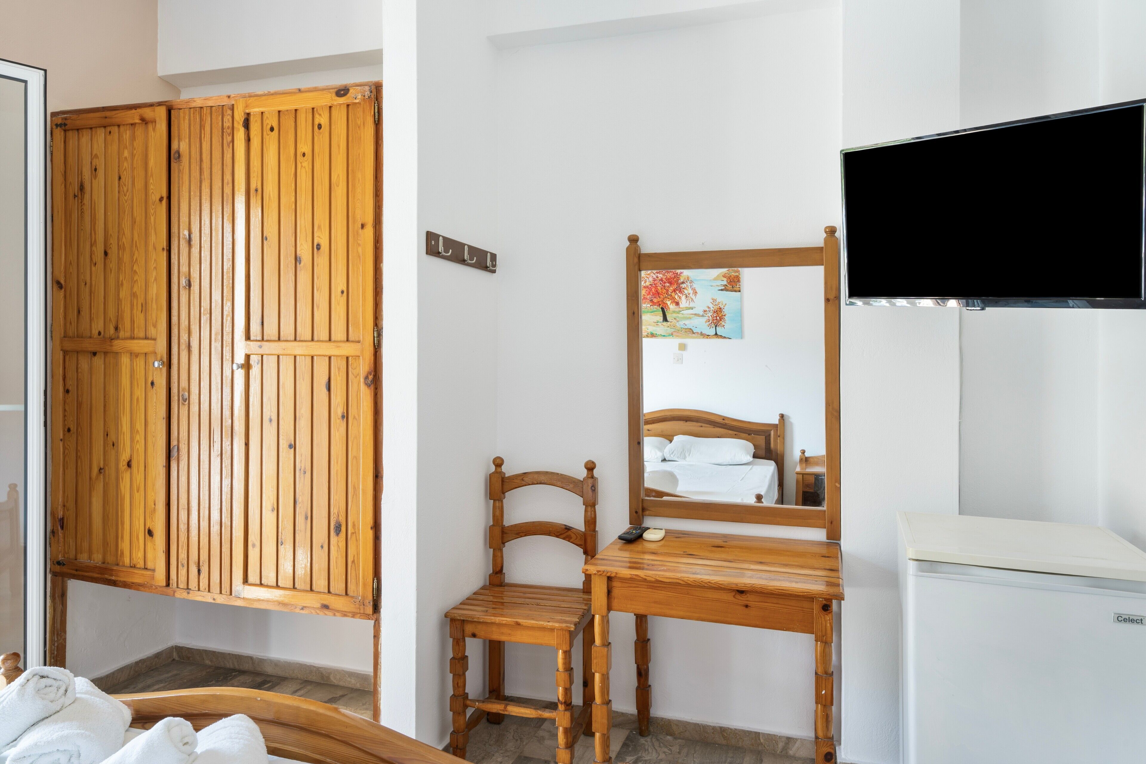 Una habitación con muebles de madera, una cama, televisor y un refrigerador pequeño.