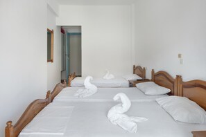 A hotel room with three beds, each with a swan towel design, wooden headboards, and white linens.