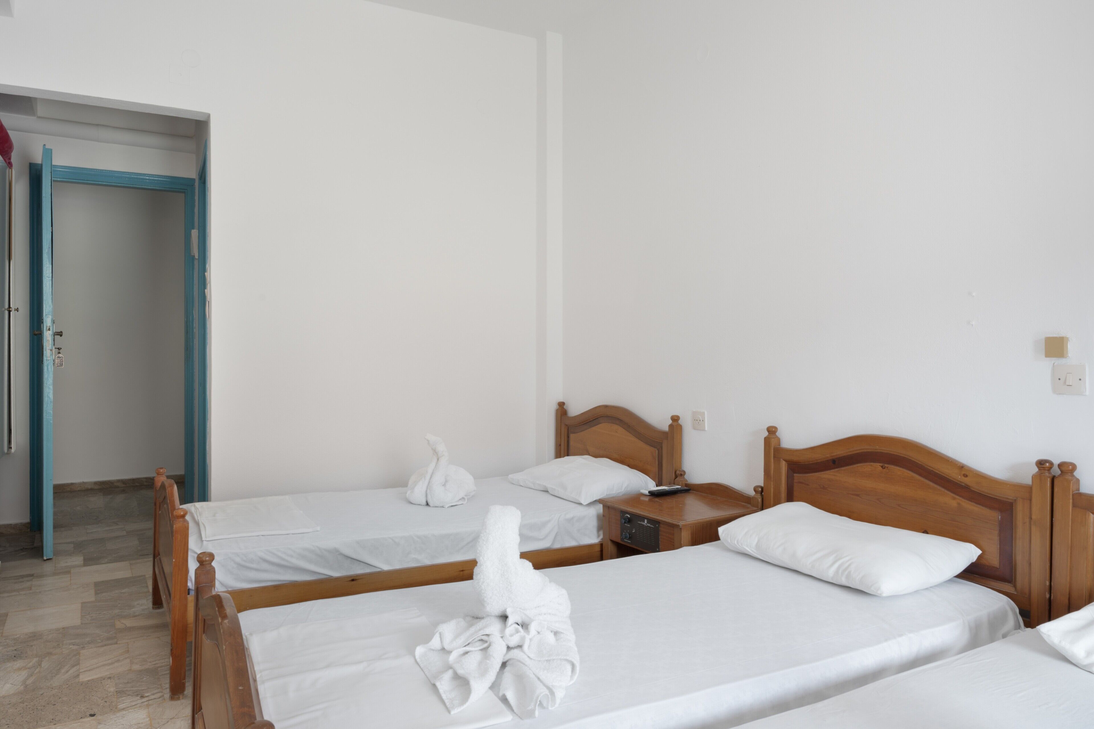 A hotel room with three wooden beds, white linens, and a wooden nightstand with a remote control.