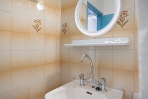 A bathroom with a white sink, a mirror, and a shelf above the sink.
