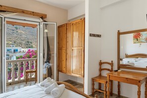 Une chambre avec un lit, des meubles en bois, un balcon donnant sur le paysage et un tableau au mur.