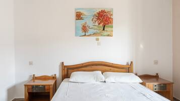A bedroom with a wooden bed, white bedding, a painting of trees, and bedside tables with radios.