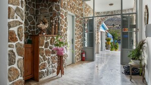 Un pasillo con paredes de piedra que conduce a una puerta de vidrio, con un extintor y una planta en maceta en el suelo.