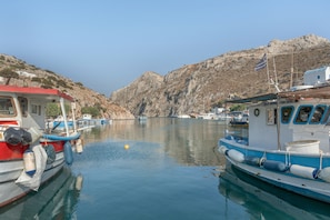 A marina with boats docked, calm water, and rocky hills in the background.