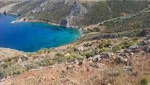 Un paisaje montañoso con mar azul cristalino, terreno rocoso y vegetación escasa.