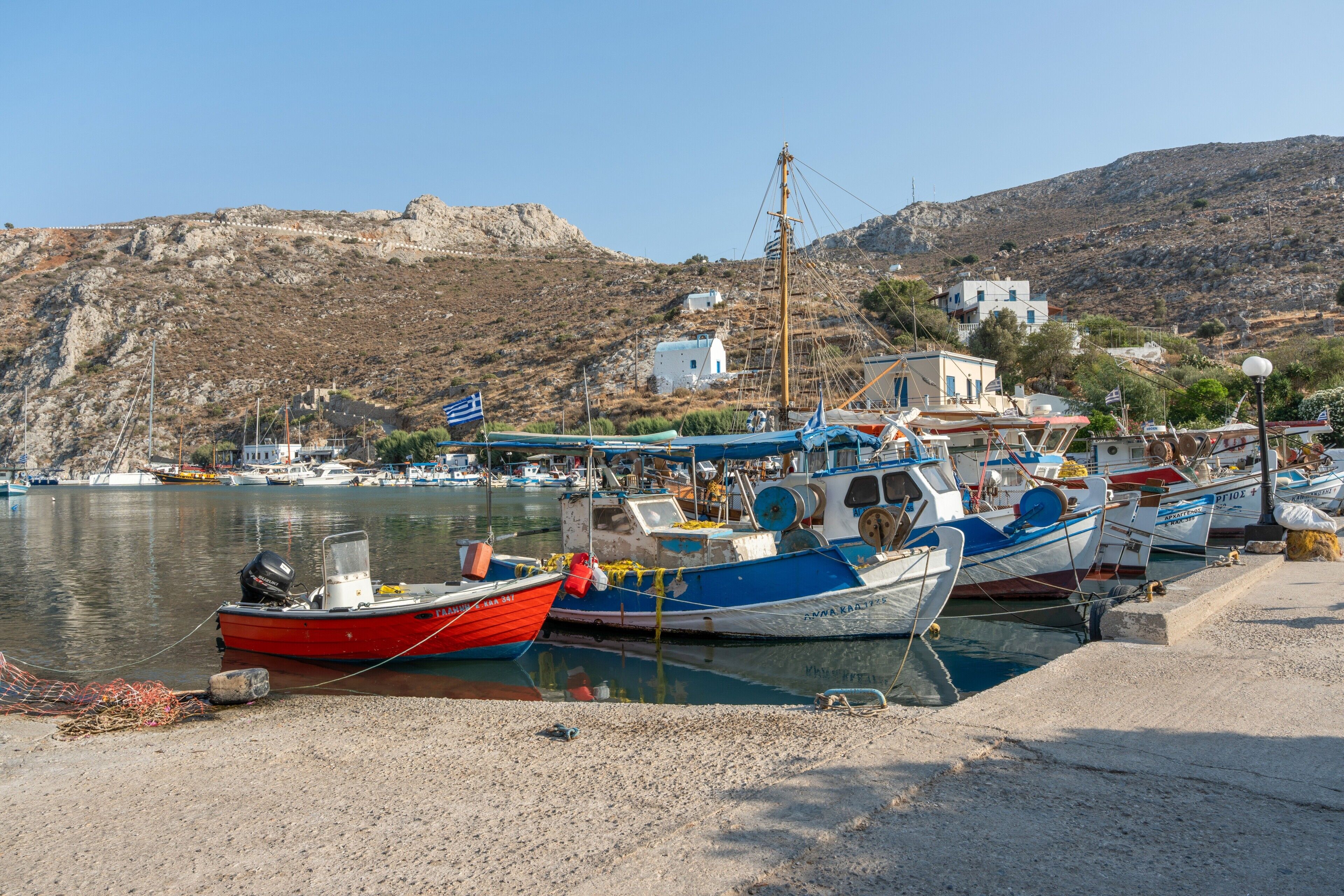Un puerto con barcos amarrados, una colina rocosa y edificios al fondo.