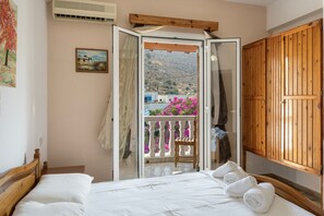 A bedroom with a bed, a wooden wardrobe, a balcony with a chair, and a painting on the wall.
