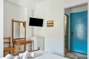 Une chambre à coucher avec un lit, une chaise en bois, un bureau, une télévision, un petit réfrigérateur et une porte bleue.