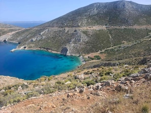 Un paysage montagneux avec une mer bleue et limpide, un terrain rocheux et une végétation clairsemée.