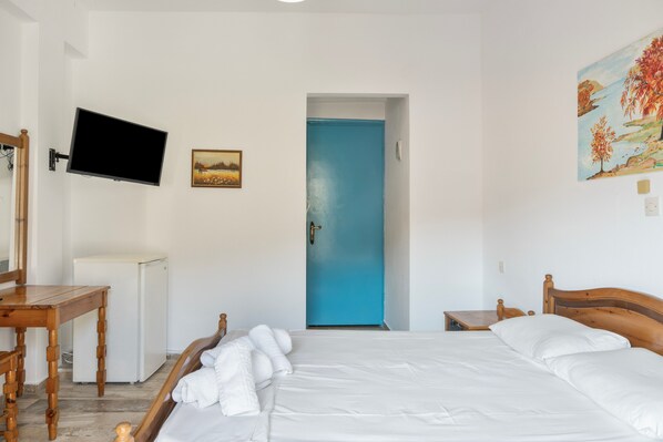 Un dormitorio con una cama, un televisor montado en la pared, un escritorio pequeño y una puerta azul.