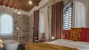 Une chambre avec une grande baignoire, un lit avec une tête de lit rouge et un mur en pierre.