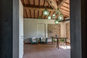 A room with a rustic ceiling, a stone wall, a white door, two teal chairs, a table with chairs, and hanging green glass lamps. - Villa 'Fattoria Mantellassi' with Private Garden, Wi-Fi and Air Conditioning (Quarrata)