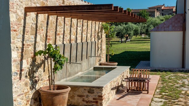 Un mur de pierre agrémenté d’une pergola en bois, une fontaine rectangulaire et un banc.